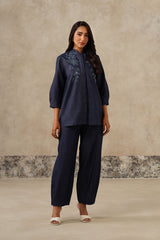 A woman modeling a denim coord set consisting of a long-sleeve embroidered top and matching wide-leg pants