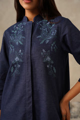 A close-up of a woman wearing a dark navy blue tunic top with light blue-green floral embroidery on the chest