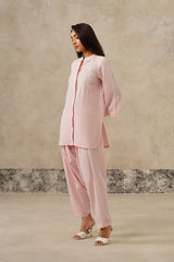 A woman models a light pink coord set outfit consisting of a long-sleeved embroidered kurta and matching dhoti style pants, floral embroidery