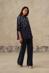 A woman wear denim embroidered coord set, consisting of a short-sleeved button-up top with intricate embroidery and matching wide-leg trousers