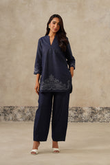 A woman modeling a denim coord set kurta set with matching wide-leg trousers, featuring a V-neckline and embroidered detailing near the hem,  cutwork embroidery